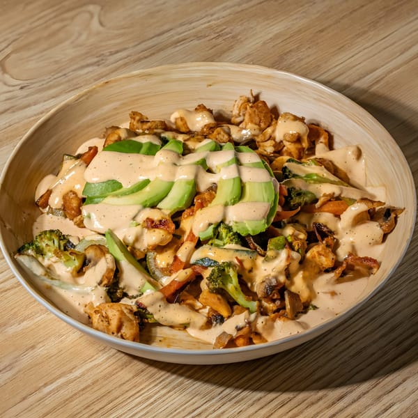 Mexican dish with chicken, vegetables, avocado slices, and creamy sauce in a wooden bowl.