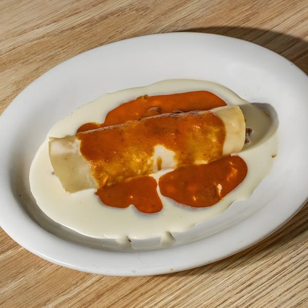 A Mexican enchilada covered in red and white sauces, served on a white oval plate.