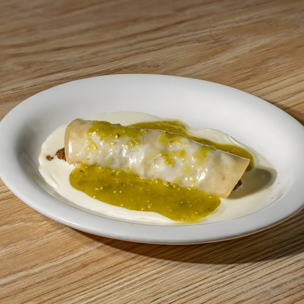A Mexican enchilada covered in green salsa and white cream sauce on a white plate.