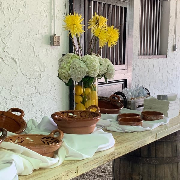 A buffet table with Mexican pottery, white linens, and floral arrangements with lemons.