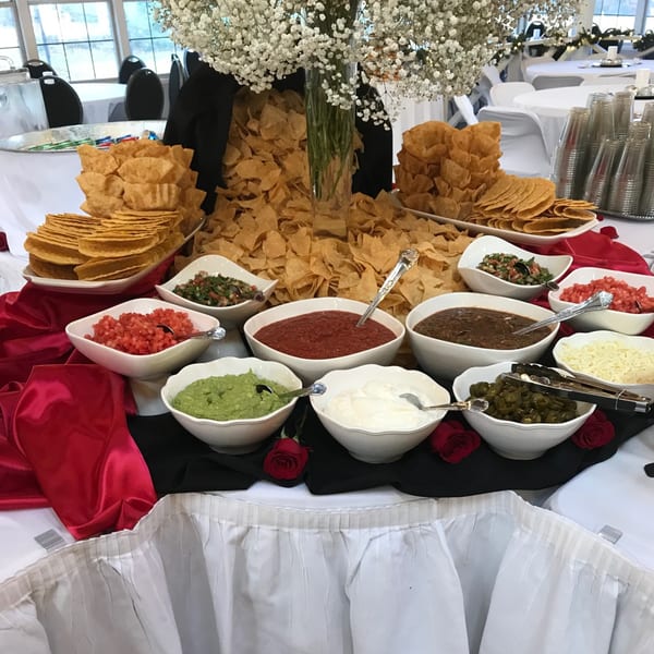 A Mexican buffet with chips, salsa, guacamole, sour cream, and other toppings on a table.