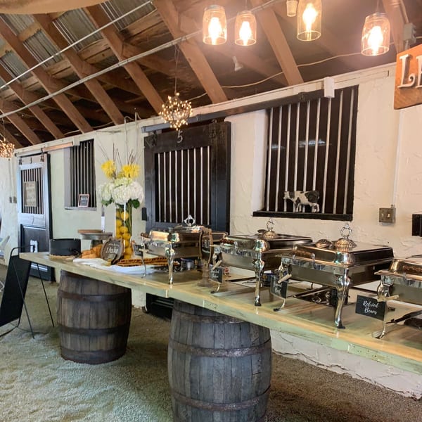A buffet table with chafing dishes and a floral arrangement, set up in a rustic barn-like room.
