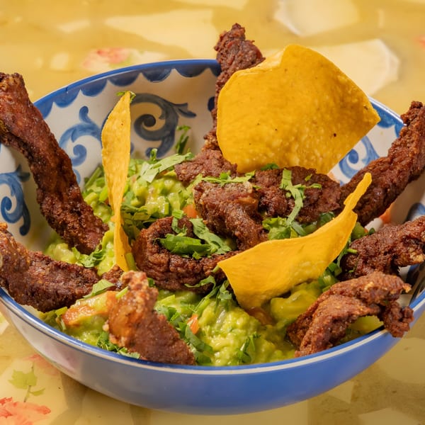 A blue and white bowl filled with guacamole, topped with crispy pork rinds and tortilla chips.