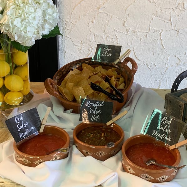 A buffet of corn chips and three types of salsa, including red medium and roasted hot.