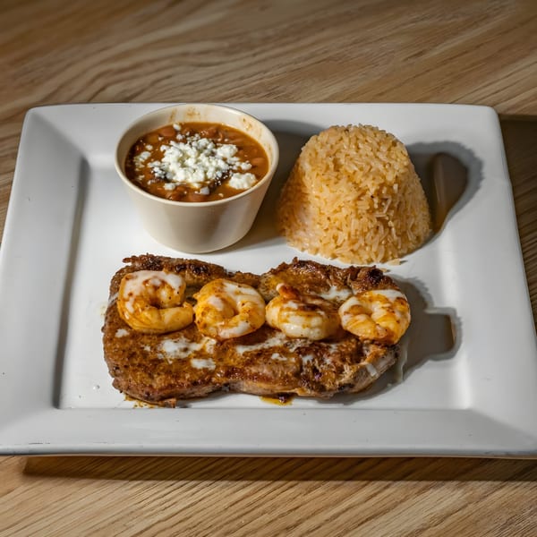 Castillo Real's steak and shrimp entree with rice and a side of beans topped with cheese.