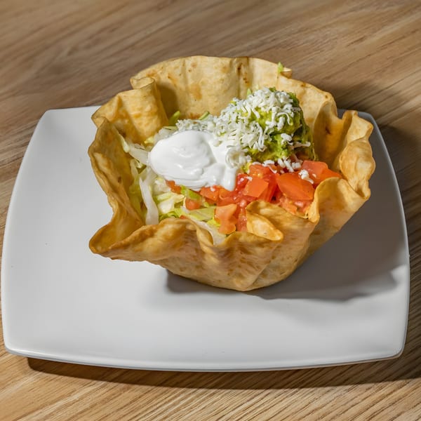 A taco salad in a crispy tortilla bowl, topped with lettuce, tomatoes, sour cream, guacamole, and cheese.