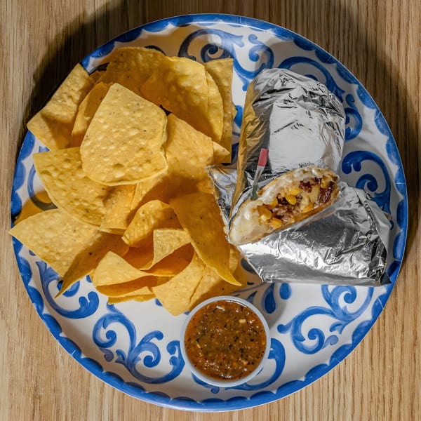 A foil-wrapped burrito, tortilla chips, and salsa on a blue and white patterned plate.