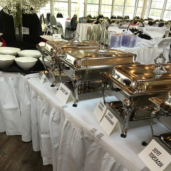 A buffet table with silver chafing dishes and white serving bowls, labeled for Mexican food.